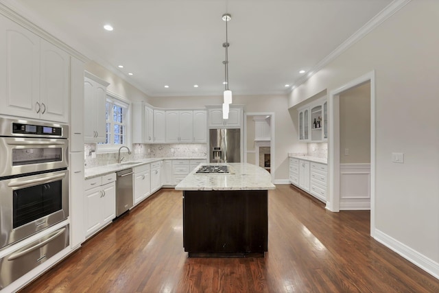 kitchen with appliances with stainless steel finishes, light stone counters, decorative light fixtures, white cabinetry, and a kitchen island