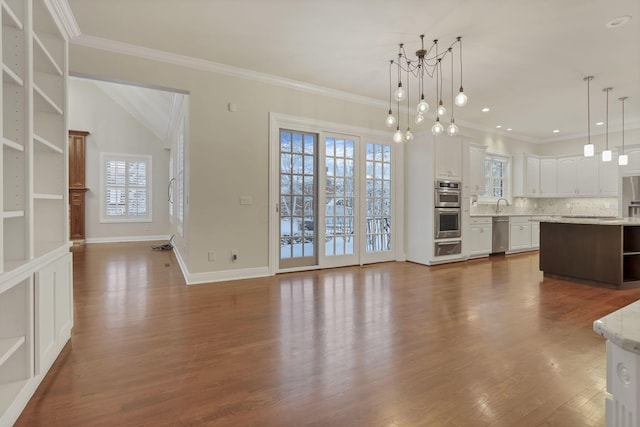 unfurnished living room with dark wood-type flooring, crown molding, plenty of natural light, and a chandelier