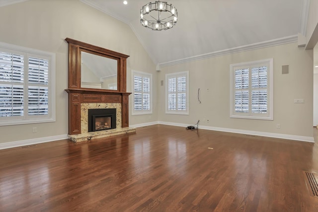 unfurnished living room featuring lofted ceiling, dark wood-type flooring, an inviting chandelier, a stone fireplace, and crown molding