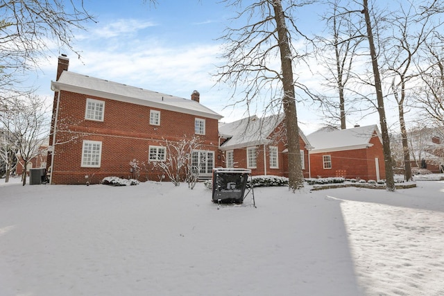 snow covered rear of property featuring central AC unit