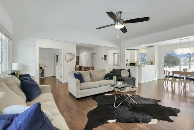 living room featuring ceiling fan with notable chandelier, plenty of natural light, and dark wood-type flooring