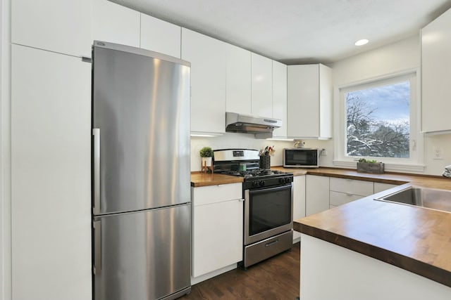 kitchen with butcher block countertops, ventilation hood, white cabinets, and appliances with stainless steel finishes