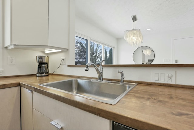 kitchen featuring an inviting chandelier, white cabinets, sink, hanging light fixtures, and a textured ceiling