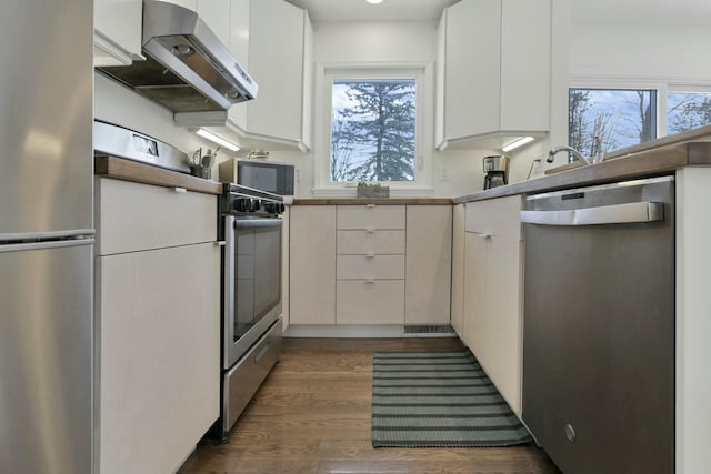 kitchen featuring appliances with stainless steel finishes, white cabinetry, dark wood-type flooring, and range hood