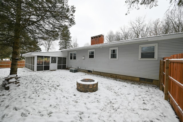 snow covered rear of property featuring a fire pit, central AC unit, and a sunroom