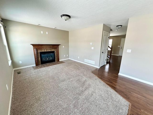 unfurnished living room with a tiled fireplace, dark hardwood / wood-style flooring, and a textured ceiling