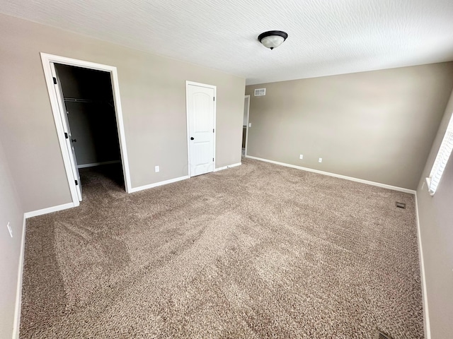 unfurnished bedroom featuring a walk in closet, carpet flooring, a textured ceiling, and a closet