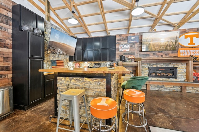 bar featuring butcher block countertops, a stone fireplace, and lofted ceiling