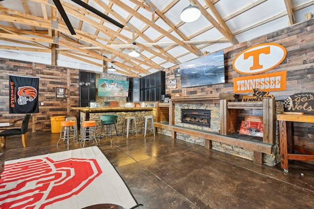 interior space featuring a stone fireplace, wooden walls, high vaulted ceiling, and indoor bar