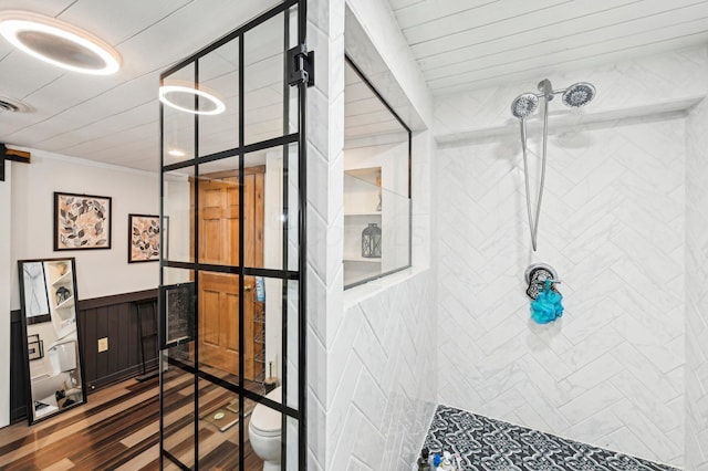 bathroom with hardwood / wood-style floors, toilet, a tile shower, and ornamental molding