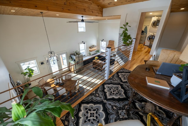 living room featuring wooden ceiling, ceiling fan with notable chandelier, stacked washer and dryer, light hardwood / wood-style flooring, and plenty of natural light