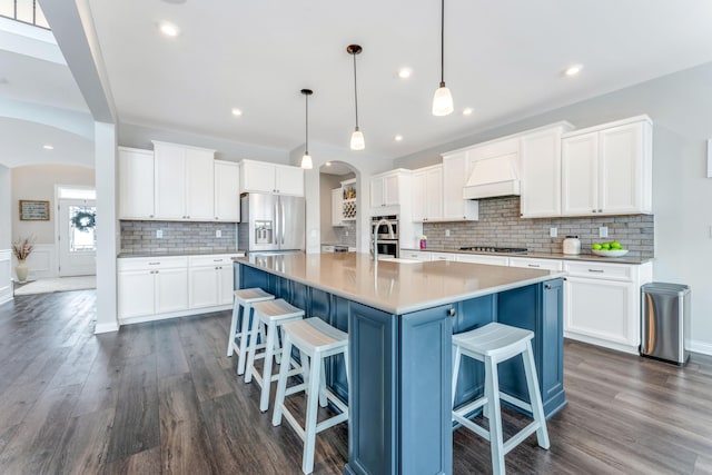 kitchen featuring white cabinets, appliances with stainless steel finishes, a center island with sink, and pendant lighting