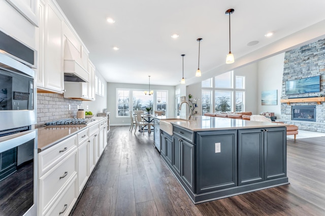 kitchen featuring decorative light fixtures, a center island with sink, white cabinetry, and a stone fireplace