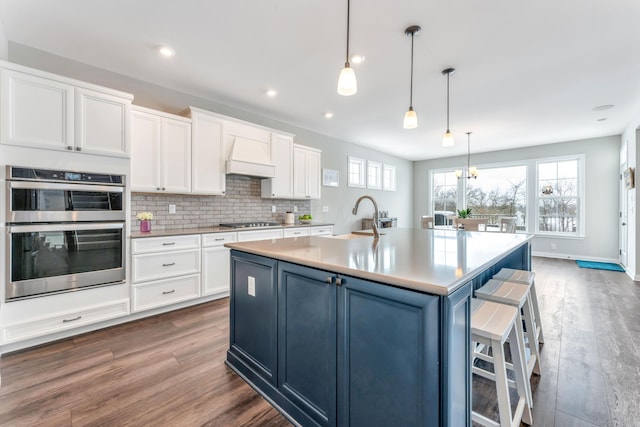 kitchen featuring white cabinetry, a kitchen island with sink, decorative light fixtures, and appliances with stainless steel finishes