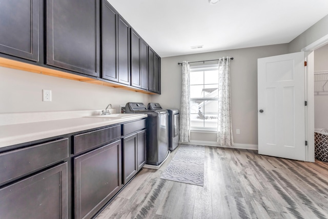 laundry area with cabinets, light wood-type flooring, sink, and washing machine and clothes dryer