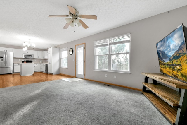 living room featuring a textured ceiling, ceiling fan with notable chandelier, and light carpet