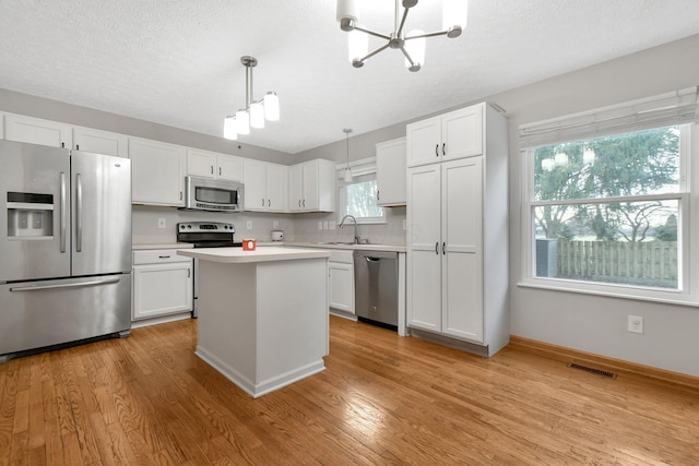 kitchen featuring white cabinetry, sink, light hardwood / wood-style flooring, decorative light fixtures, and appliances with stainless steel finishes