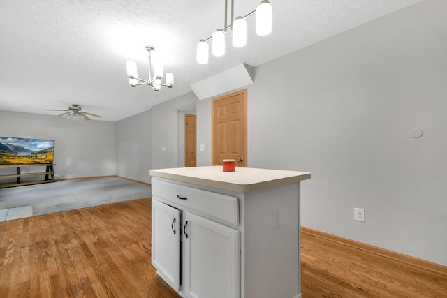 kitchen with ceiling fan with notable chandelier, light hardwood / wood-style flooring, decorative light fixtures, a kitchen island, and white cabinetry