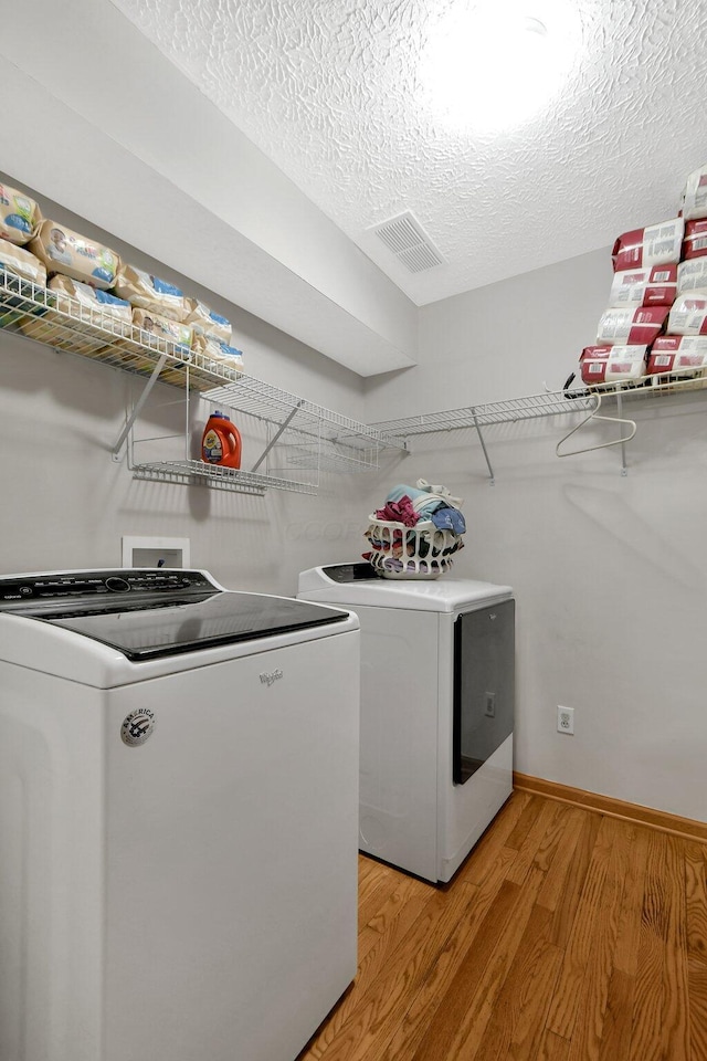 laundry area with washing machine and clothes dryer, a textured ceiling, and light wood-type flooring