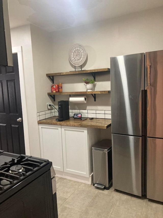 kitchen with black range, wood counters, stainless steel fridge, and white cabinetry