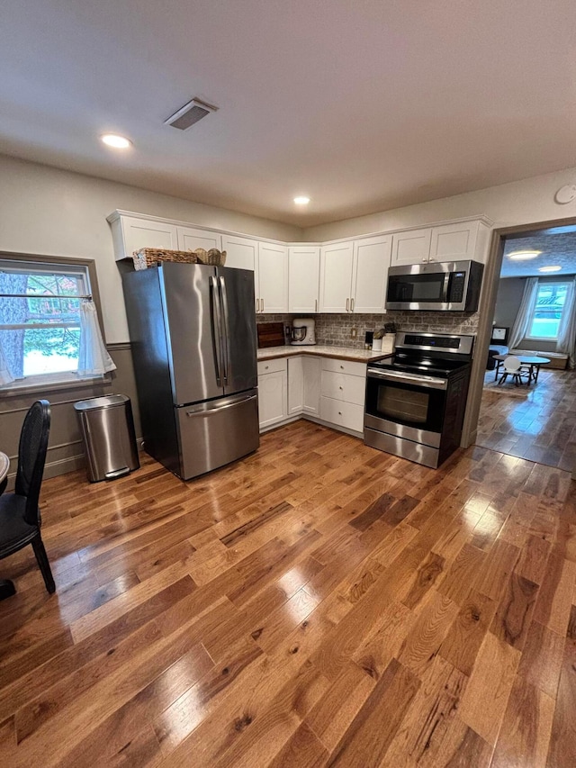 kitchen featuring decorative backsplash, white cabinets, stainless steel appliances, and wood-type flooring