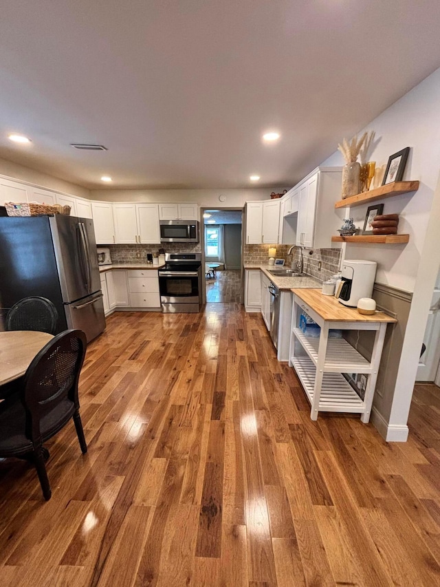 kitchen featuring white cabinets, sink, light hardwood / wood-style flooring, decorative backsplash, and stainless steel appliances