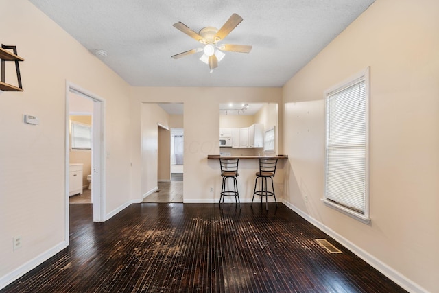 interior space with white cabinets, kitchen peninsula, ceiling fan, wood-type flooring, and a breakfast bar area