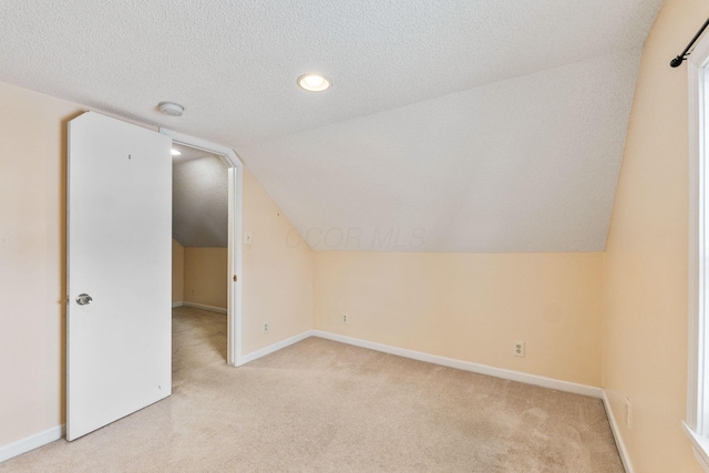 additional living space with light carpet, a textured ceiling, and vaulted ceiling