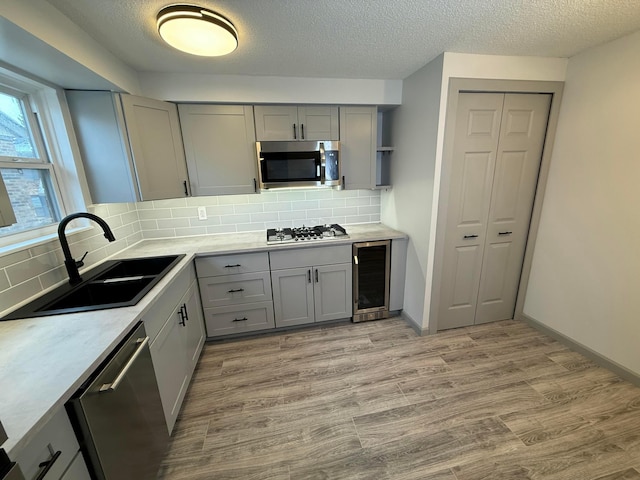 kitchen with decorative backsplash, appliances with stainless steel finishes, beverage cooler, sink, and gray cabinets