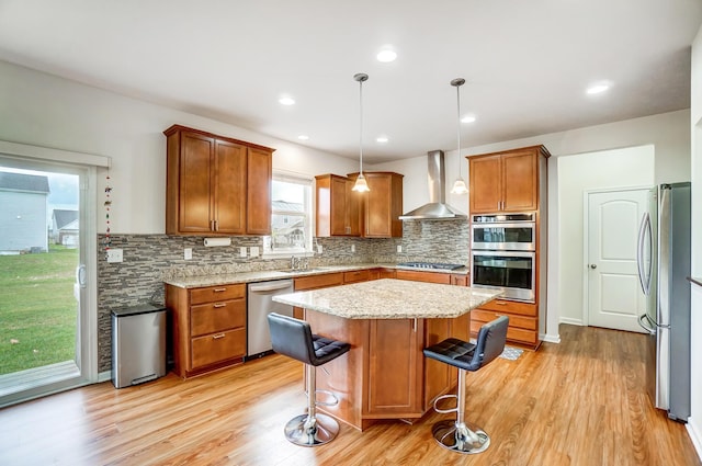 kitchen with stainless steel appliances, wall chimney range hood, pendant lighting, a kitchen island, and a breakfast bar area