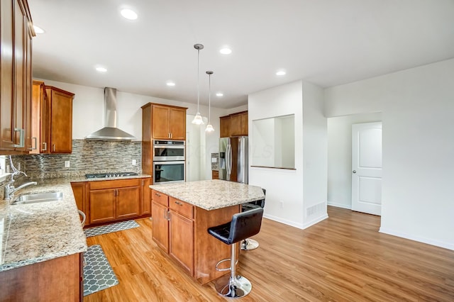 kitchen featuring a center island, wall chimney exhaust hood, hanging light fixtures, sink, and appliances with stainless steel finishes