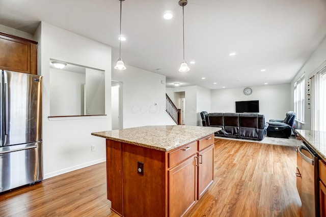 kitchen featuring light stone countertops, appliances with stainless steel finishes, decorative light fixtures, light hardwood / wood-style flooring, and a center island