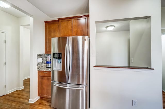 kitchen featuring backsplash, stainless steel fridge, hardwood / wood-style floors, and light stone counters