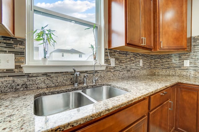 kitchen with backsplash, light stone countertops, and sink