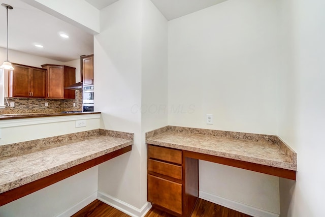 kitchen featuring dark wood-type flooring, backsplash, double oven, pendant lighting, and built in desk