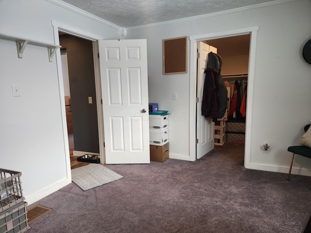 unfurnished bedroom with a spacious closet, dark colored carpet, crown molding, a textured ceiling, and a closet