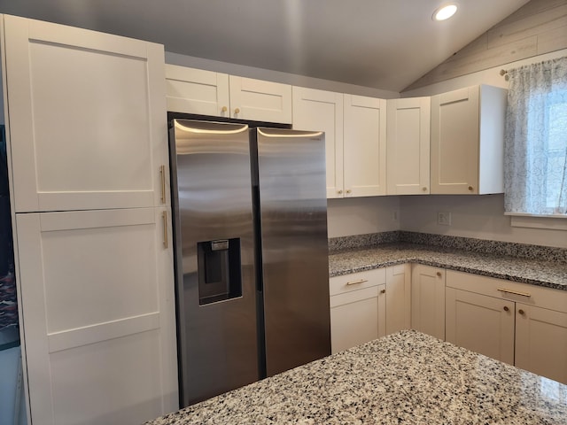 kitchen featuring white cabinetry, light stone countertops, stainless steel fridge with ice dispenser, and vaulted ceiling