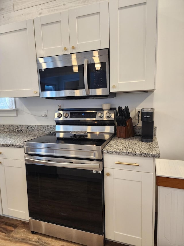 kitchen with white cabinets, light hardwood / wood-style floors, light stone countertops, and stainless steel appliances