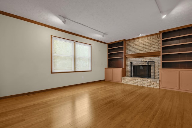 unfurnished living room featuring a fireplace, built in features, a textured ceiling, and track lighting