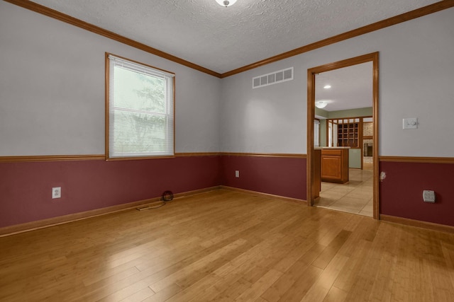 spare room featuring crown molding, a textured ceiling, and light wood-type flooring