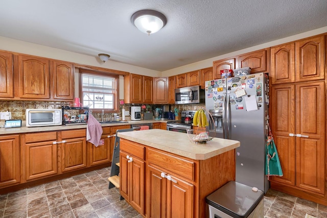 kitchen featuring decorative backsplash, appliances with stainless steel finishes, a textured ceiling, sink, and a center island