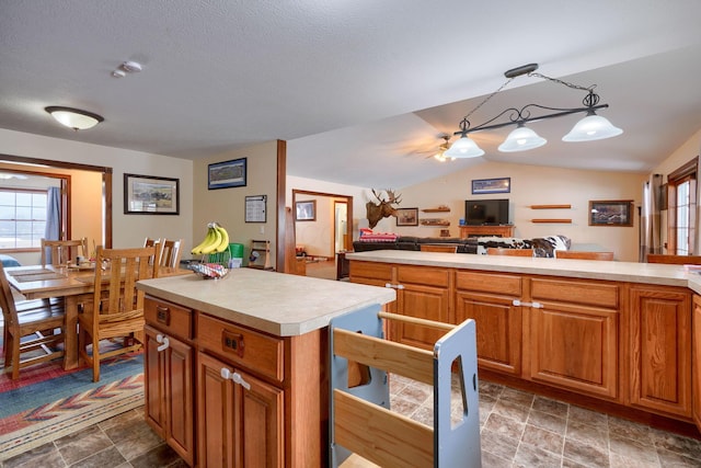 kitchen featuring a textured ceiling, a kitchen island, hanging light fixtures, and vaulted ceiling