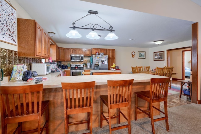 kitchen featuring hanging light fixtures, backsplash, kitchen peninsula, a breakfast bar area, and appliances with stainless steel finishes