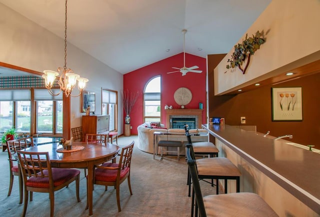 dining room with carpet, ceiling fan with notable chandelier, high vaulted ceiling, and a healthy amount of sunlight