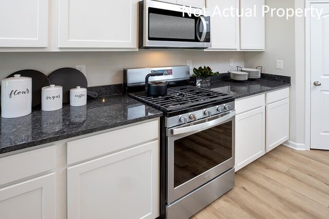 kitchen featuring stainless steel appliances, dark stone counters, white cabinets, and light wood-style flooring