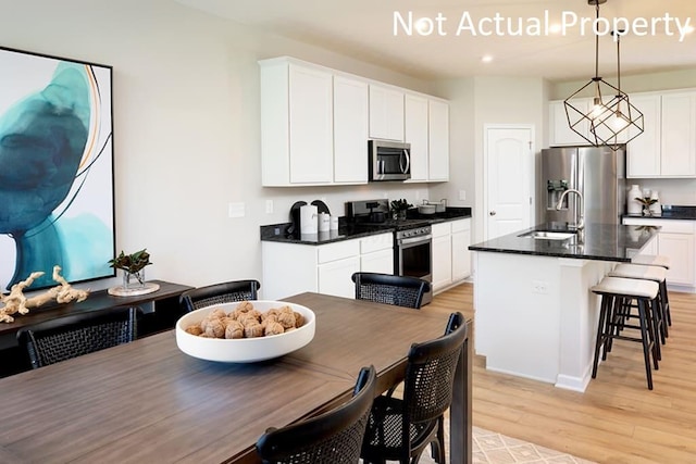 kitchen featuring dark countertops, hanging light fixtures, a kitchen island with sink, stainless steel appliances, and a sink