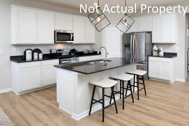kitchen featuring stainless steel appliances, a sink, white cabinets, an island with sink, and pendant lighting