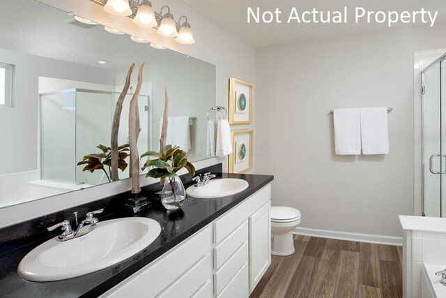 full bathroom with double vanity, a shower stall, a sink, and wood finished floors