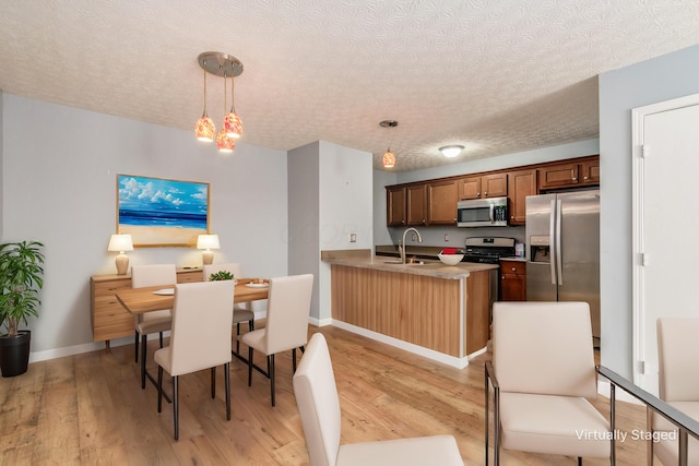 kitchen with sink, kitchen peninsula, a textured ceiling, decorative light fixtures, and appliances with stainless steel finishes