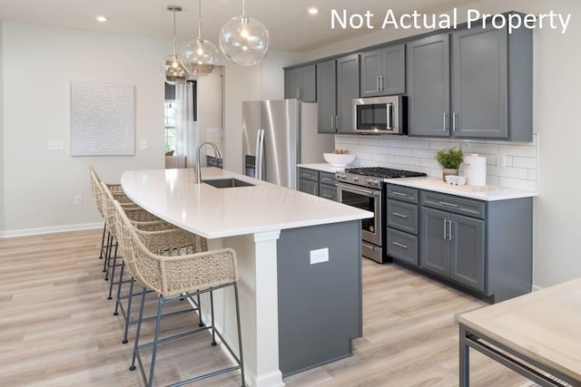 kitchen with stainless steel appliances, gray cabinetry, a center island with sink, and sink